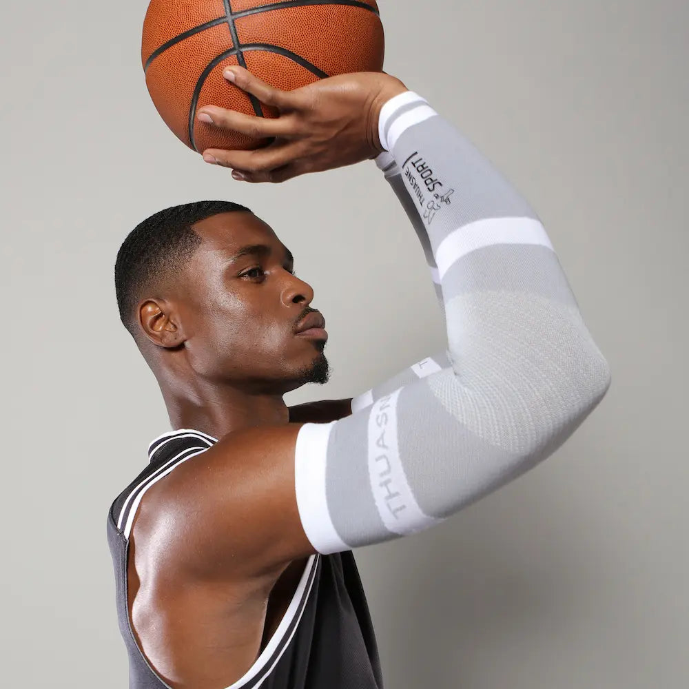 Basketteur en position de tir portant les manchettes de bras gris clair et blanc THUASNE SPORT