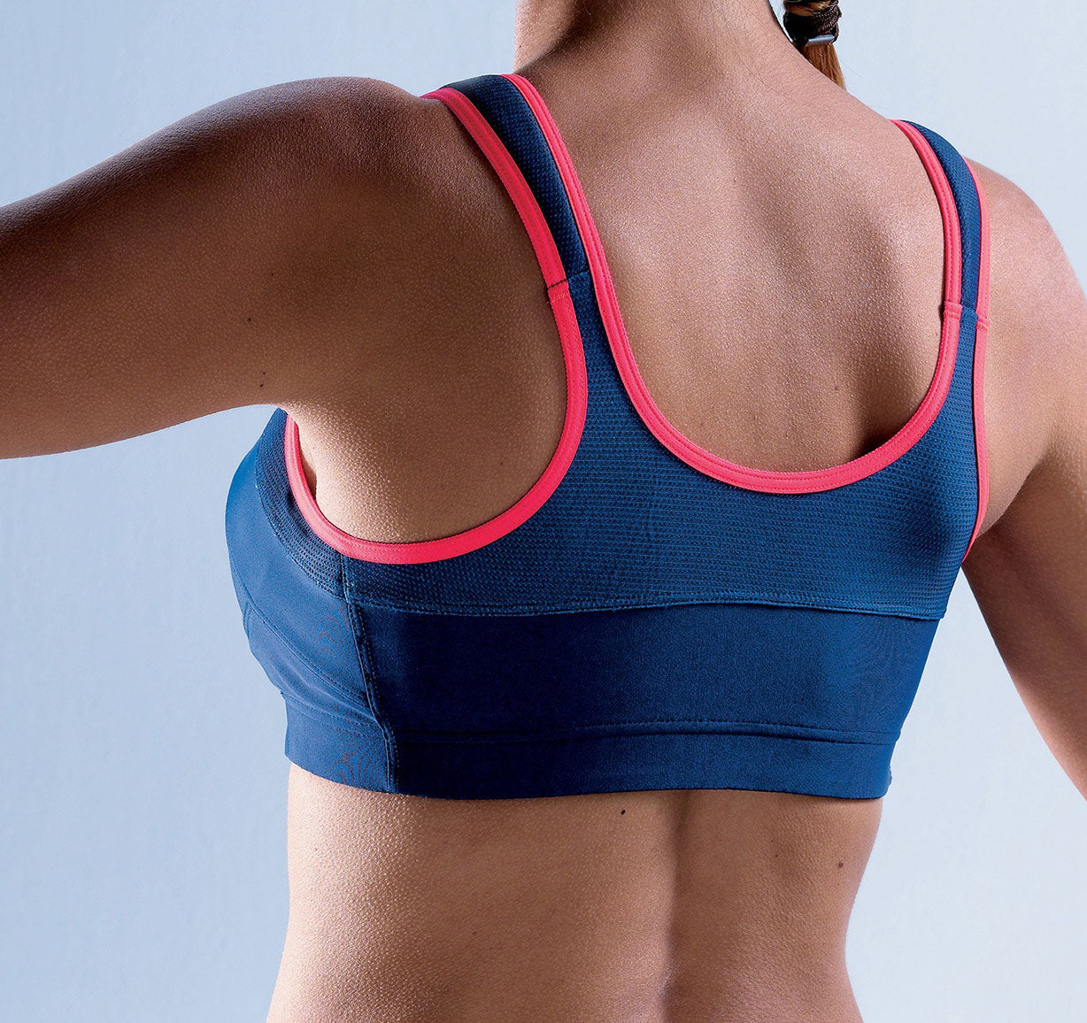 Brassière Top' Strap Fit Thuasne Sport bleu marine et rose portée par une femme, vue de dos